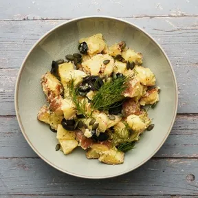 Foto van een bord met aardappelsalade met olijven, kappertjes en dille