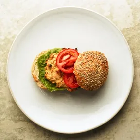 Foto van een burger van witte bonen en aardappel op een broodje met sla en tomaat