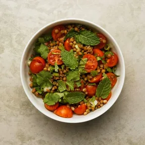 Foto van een kommetje linzentabbouleh met cherrytomaat, lente-ui en kruiden. Naar recept van Jamie Oliver.
