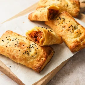 Foto van vegan zoete aardappel en gekaramelliseerde ui in bladerdeeg op een plankje